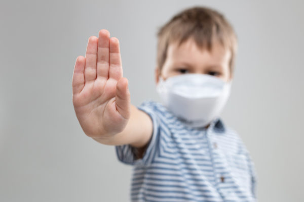 young-child-wearing-a-respiratory-mask-as-a Young Child wearing a respiratory mask and hold his hand up in a stop
