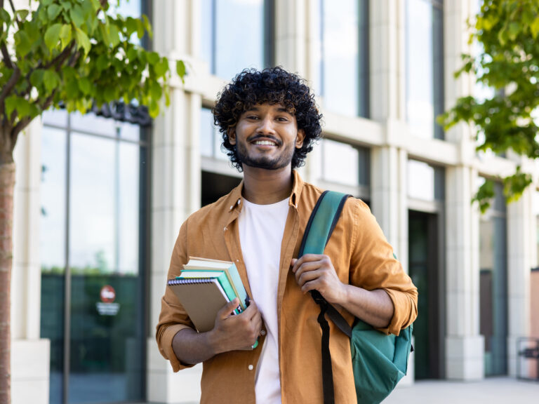 Confident male student at college, holding books and backpack.