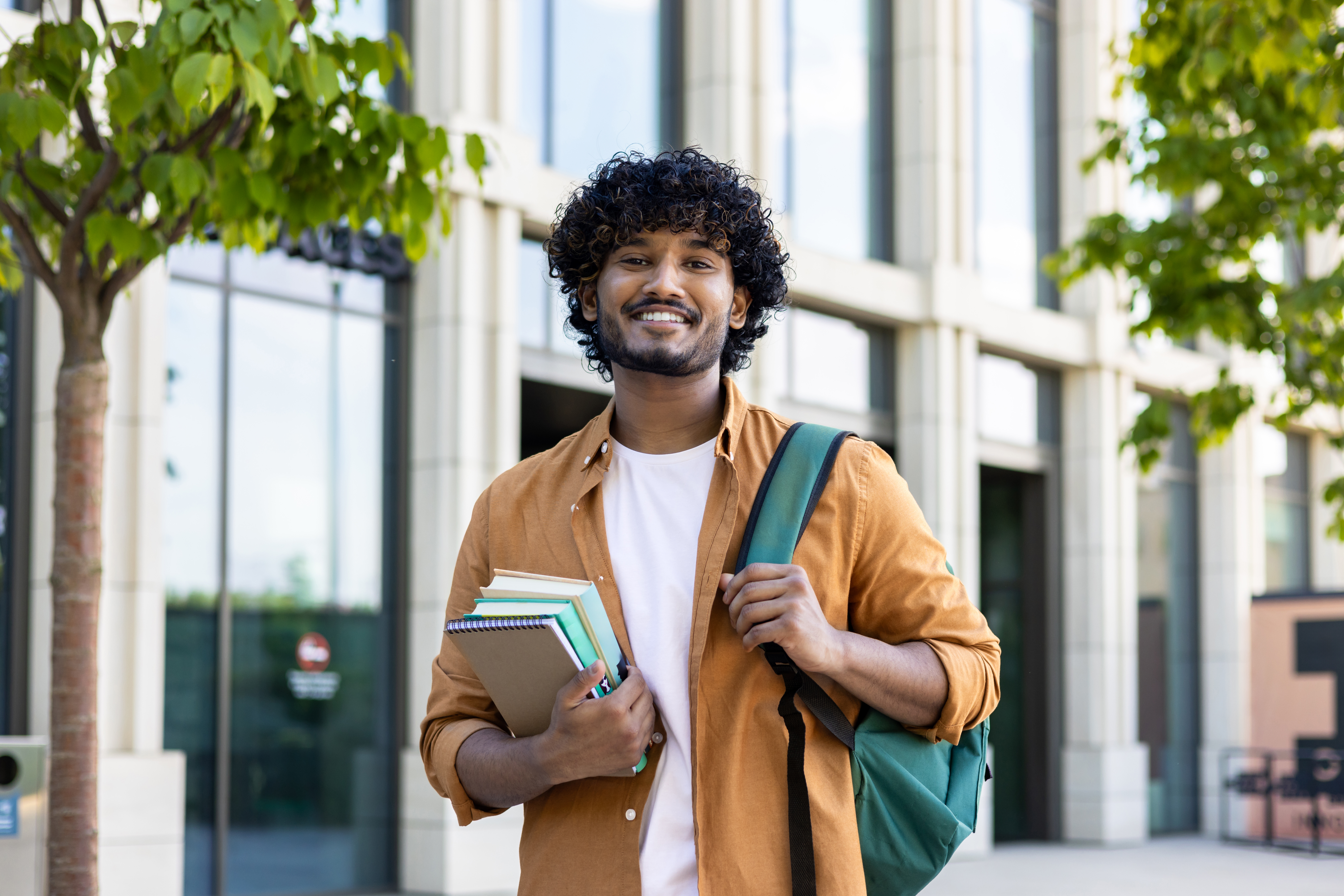 Portrait of a male college student Confident male student at college, holding books and backpack.
